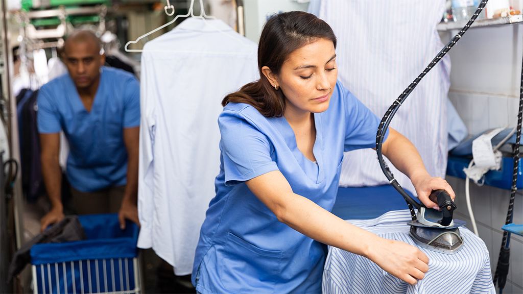 A professional at a dry cleaning service providing expert care as she irons a shirt, reflecting the skills of the people who work there.