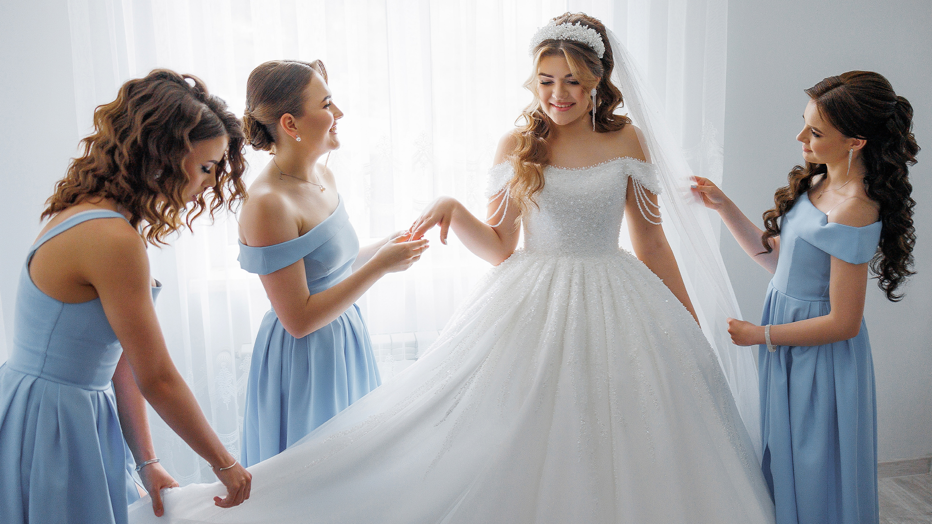 Image of a bride surrounded by her bridesmaids dressed in blue dresses, arranging her veil and gown